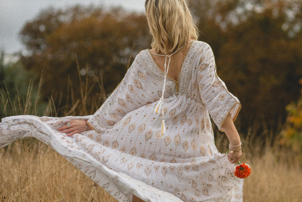 Cinematic branding photo of wellness coach in flowing dress, natural outdoor setting.