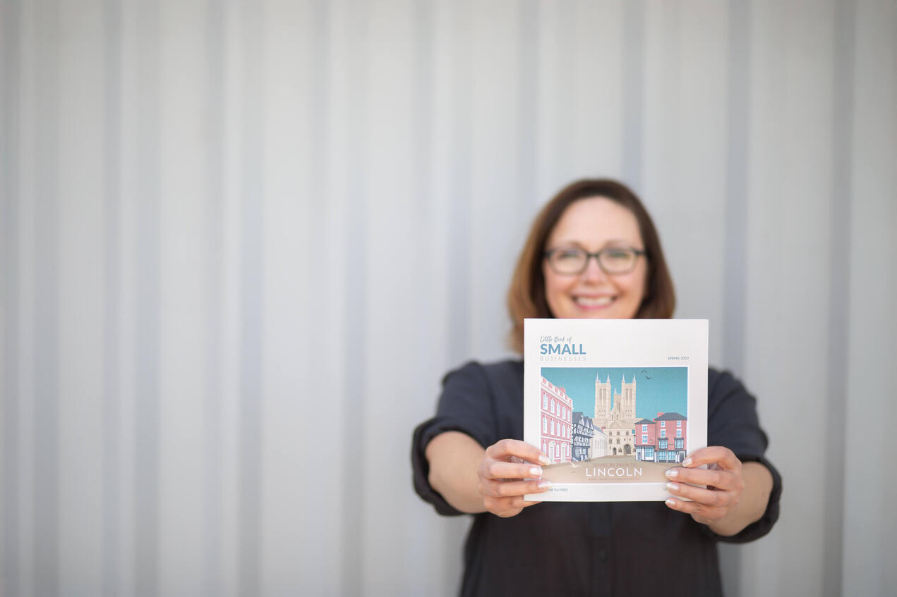 Brand photo of a publisher holding her business booklet towards the camera, with herself blurred in the background.