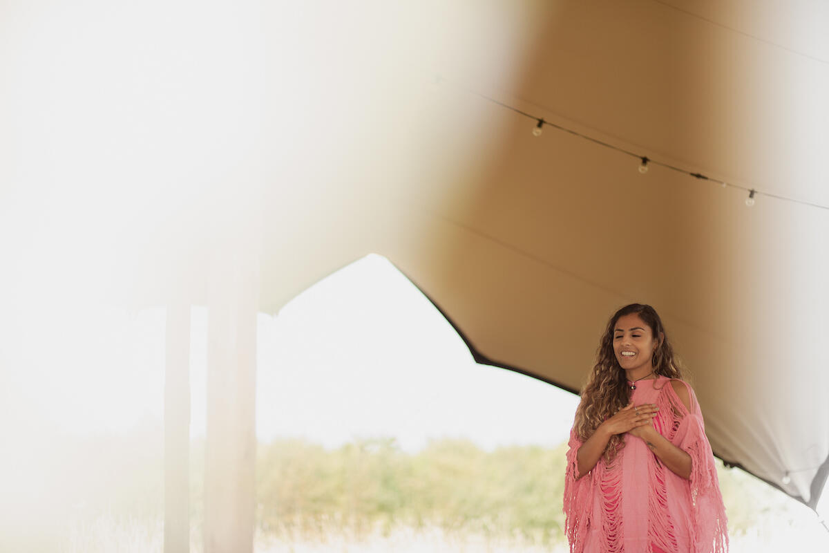 Cinematic brand photography of a retreat facilitator with eyes closed, hand on heart, guiding a moment of reflection under a tent.